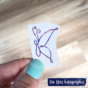 Puede incluir: Una pegatina de mariposa hologr&aacute;fica con un dise&ntilde;o geom&eacute;trico lila. La pegatina est&aacute; sobre un fondo blanco.