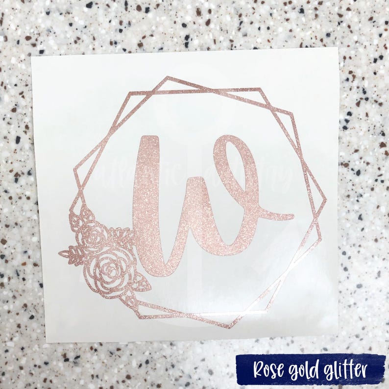 K&ouml;nnte beinhalten: Aufkleber aus ros&eacute;goldfarbenem Glitzer mit dem Buchstaben W in einem geometrischen Rahmen mit floralen Akzenten.
