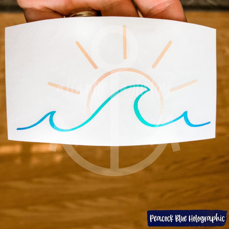 May include: A sticker with a blue and green wave and a peach colored sun with rays. The sticker is on a white background. The text "Peacock Blue Holographic" is visible in the bottom right corner of the image.