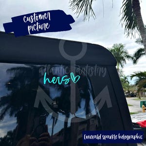 May include: A teal blue car window decal with the word "hers" and a heart. The decal is on a black car window. The decal is made with emerald sparkle holographic vinyl.