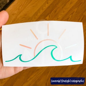 May include: A green wave with a pink and orange sun setting behind it. The design is on a white background.  Emerald Starlight Holographic.