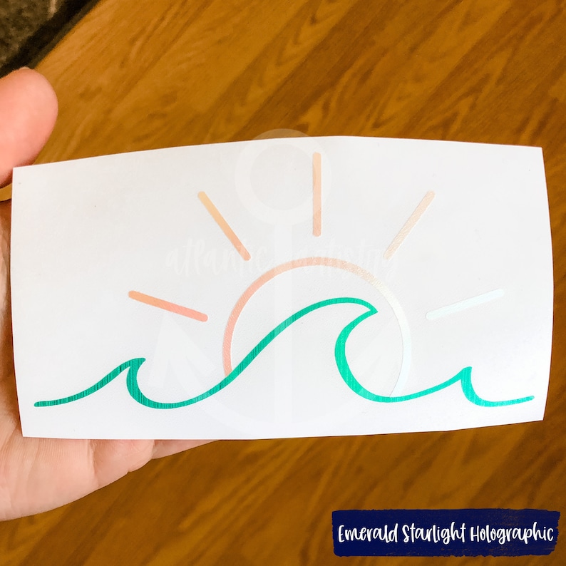 May include: A green wave with a pink and orange sun setting behind it. The design is on a white background.  Emerald Starlight Holographic.
