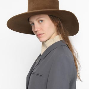 May include: A wide-brimmed hat in brown, featuring a tall crown. The hat is made from felt and has a smooth finish.