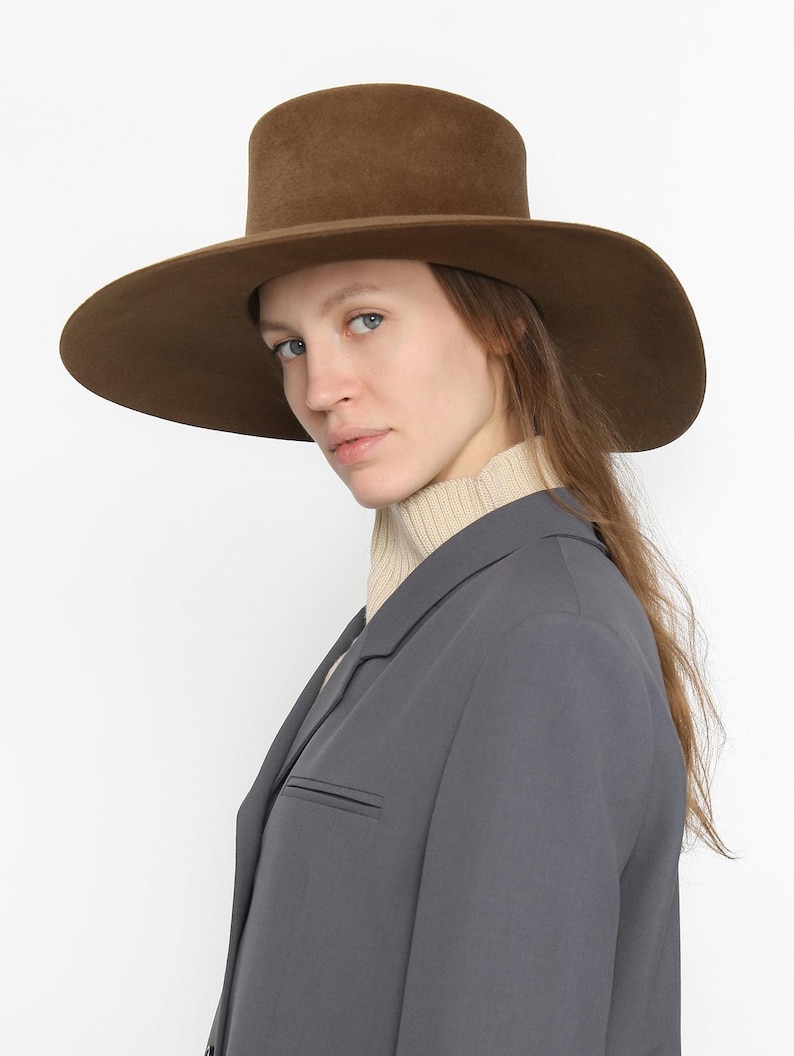 May include: A wide-brimmed hat in brown, featuring a tall crown. The hat is made from felt and has a smooth finish.
