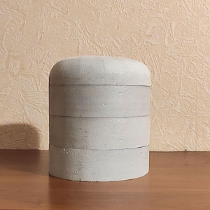 Könnte beinhalten: Ein weißer, runder, mehrschichtiger Aufbewahrungsbehälter mit einer glatten, leicht strukturierten Oberfläche. Der Behälter ist aus Holz und hat ein schlichtes, minimalistisches Design.