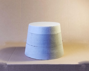 May include: A light blue, cylindrical, handmade object with a flat top and a slightly wider base. The object has a textured surface and appears to be made of concrete or a similar material. The design includes horizontal lines around the body.