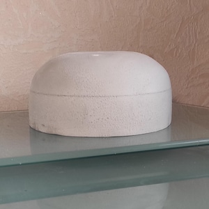 May include: A white ceramic bowl with a smooth, rounded surface. The bowl is sitting on a glass surface.