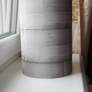 May include: A grey cylindrical planter made of stacked foam rings. The planter has a rough, textured surface.