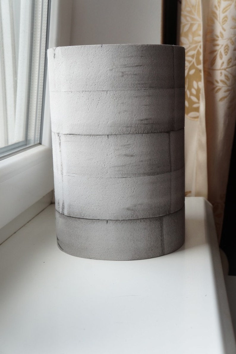 May include: A grey cylindrical planter made of stacked foam rings. The planter has a rough, textured surface.