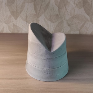 May include: A light gray, heart-shaped concrete sculpture. The sculpture has a layered design with a curved top and a rounded base. The object is sitting on a wooden surface.
