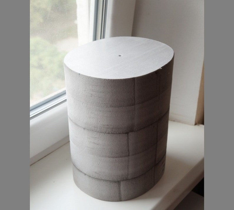 May include: A grey foam cylinder with a grid pattern on the surface. The cylinder is approximately 25 cm tall and 15 cm in diameter.