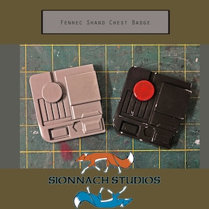 May include: Two painted plastic replicas of a Star Wars character's chest badge. One is grey with a red circle, the other is black with a red circle. The text "FENNEC SHAND CHEST BADGE" is above the badges. The text "SIONNACH STUDIOS" is below the badges.
