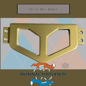 May include: A gold-colored metal belt buckle with a geometric design. The buckle has two holes on each side for attaching a belt.