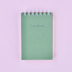 May include: A green spiral bound notebook with the words "Brain Dump" written on the front cover.