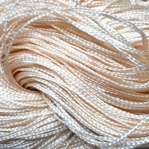 Puede incluir: Primer plano de una gran bobina de hilo de color crema. El hilo está enrollado apretado y tiene una textura suave y sedosa.