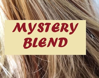 May include: A close-up of a blend of blonde, light brown, and dark brown human hair extensions. The hair is arranged in a loose, wavy style. The text "MYSTERY BLEND" is printed on a yellow label.