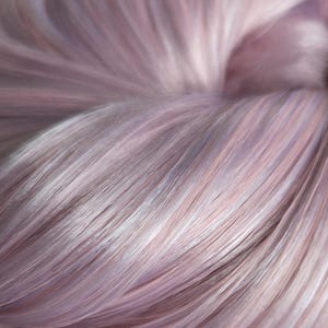 May include: A skein of yarn featuring a soft blend of pastel lavender, pale pink, and muted blue fibres. The strands are tightly twisted together, creating a smooth, lustrous texture with a subtle sheen that reflects light across the surface.