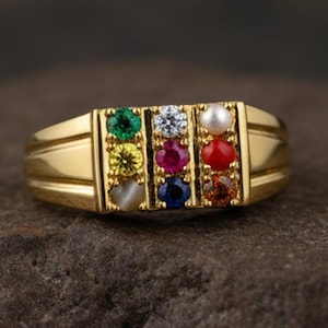 May include: A gold ring with a rectangular setting displaying a series of colourful gemstones. The gemstones are green, yellow, white, pink, blue, red, and brown. The ring has a traditional band design.