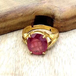 May include: A gold ring with a large, oval-shaped, pink gemstone set in the center. The ring has a simple, elegant design.