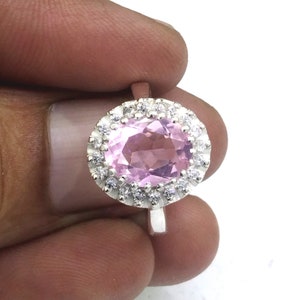 以下が含まれることがあります： 大きなピンクの楕円形の宝石が、小さな白い宝石で囲まれたシルバーリング