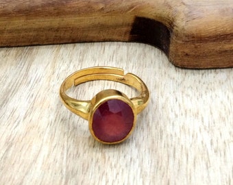 May include: A gold ring with a round, red gemstone. The ring is on a wooden surface.