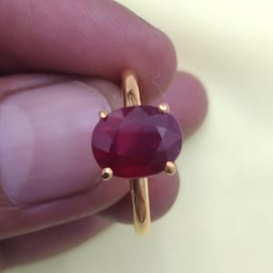 Puede incluir: Un anillo de oro con una gran piedra preciosa de rubí de forma ovalada.