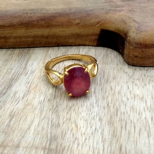 May include: A gold ring with a large, oval-shaped, pink gemstone set in the center. The ring has a simple, elegant design.
