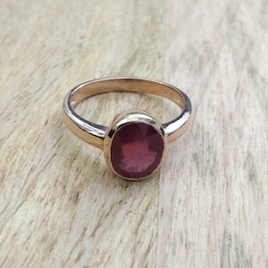 Könnte beinhalten: Ein Ring aus Roségold mit einem tief roten ovalen Edelstein.