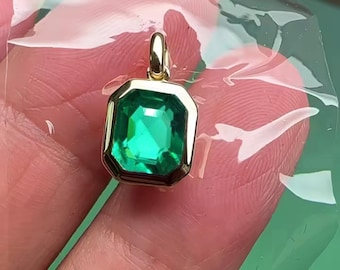 May include: A gold pendant with a square emerald green gemstone.