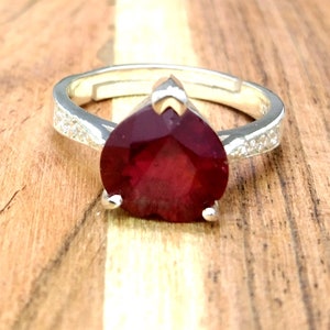 May include: A silver ring with a large, red, heart-shaped gemstone and a band of small, clear gemstones.