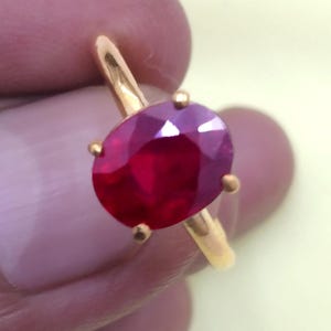 May include: A gold ring with a large, oval-shaped ruby gemstone. The ruby is a deep red color and has a high polish.