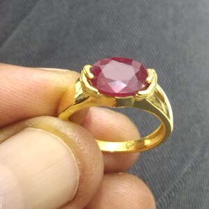 Op de afbeelding: Een gouden ring met een grote, ovale robijn-edelsteen. De robijn is dieprood en heeft een facetgeslepen vorm.