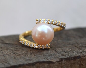 May include: A gold ring featuring a large, off-white pearl and a band of small, clear stones.