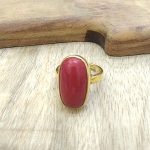 May include: A gold ring with a large, oval-shaped red gemstone.
