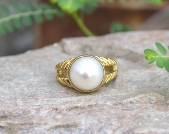 May include: A gold ring with a white pearl set in the centre. The ring has a twisted rope design on the band.
