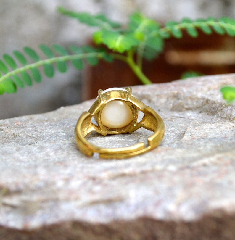 May include: A gold ring with a white oval-shaped stone set in the centre. The ring is adjustable and has a simple design.