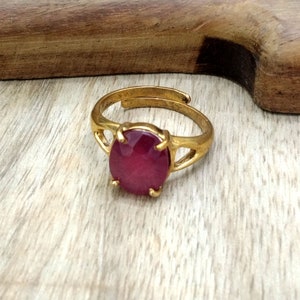 Op de afbeelding: Een gouden ring met een grote, ronde, donkerroze edelsteen. De ring ligt op een houten oppervlak.