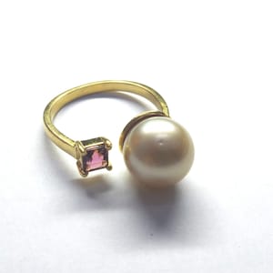 Könnte beinhalten: Ein goldener Ring mit einer großen weißen Perle und einem kleinen quadratischen rosafarbenen Edelstein.