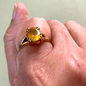 May include: A gold ring with a large, oval-shaped, yellow gemstone.