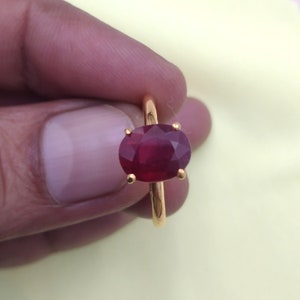 May include: A gold ring featuring a large, oval-shaped ruby gemstone. The ruby is a deep red colour and is set in a simple, gold band.
