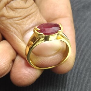 Peut inclure: Une bague en or avec une grande pierre précieuse de rubis de forme ovale. La bague a un design simple avec une bande lisse.