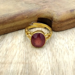 May include: A gold ring with a large, oval-shaped, dark red gemstone.