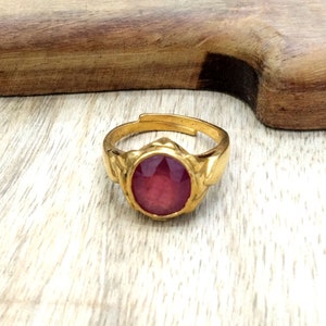 May include: A gold ring with a large, round, red gemstone set in a decorative, floral-shaped setting.