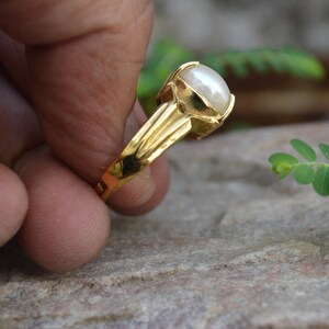 May include: A gold ring featuring a large, white pearl set in the centre. The ring has a simple, elegant design.