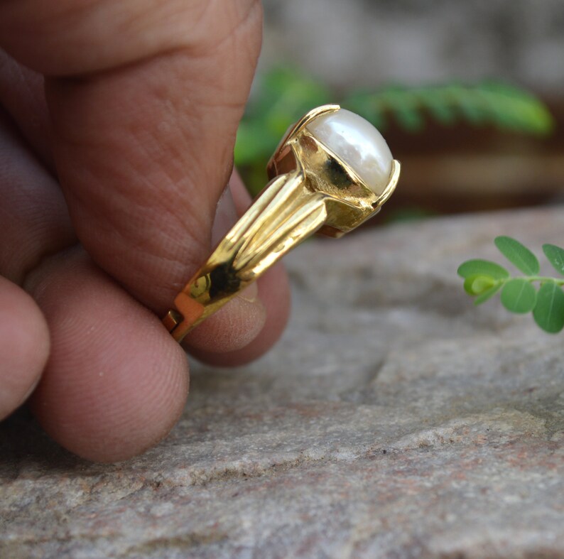 May include: A gold ring featuring a large, white pearl set in the centre. The ring has a simple, elegant design.