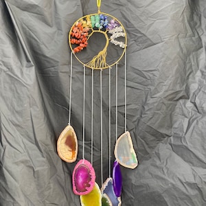 May include: A handcrafted wind chime featuring a gold-colored wire tree of life design adorned with colorful gemstones. Below, seven agate slices in various colors hang from the tree, creating a decorative and spiritual piece.