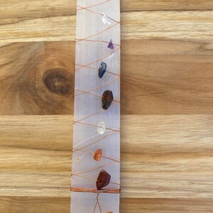 May include: A selenite charging plate with copper wire wrapped around it. There are seven different colored crystals placed on the plate, including clear, purple, blue, brown, clear, orange, and red.