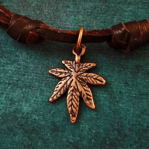 May include: A brown leather cord necklace with a copper-colored marijuana leaf pendant.