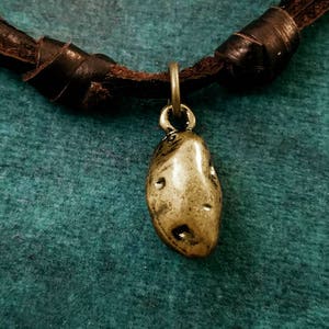 May include: A brown leather cord necklace with a gold-colored potato charm. The necklace is on a teal background.