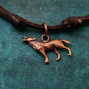 May include: A brown leather necklace with a copper wolf pendant. The wolf is howling and has a detailed design.